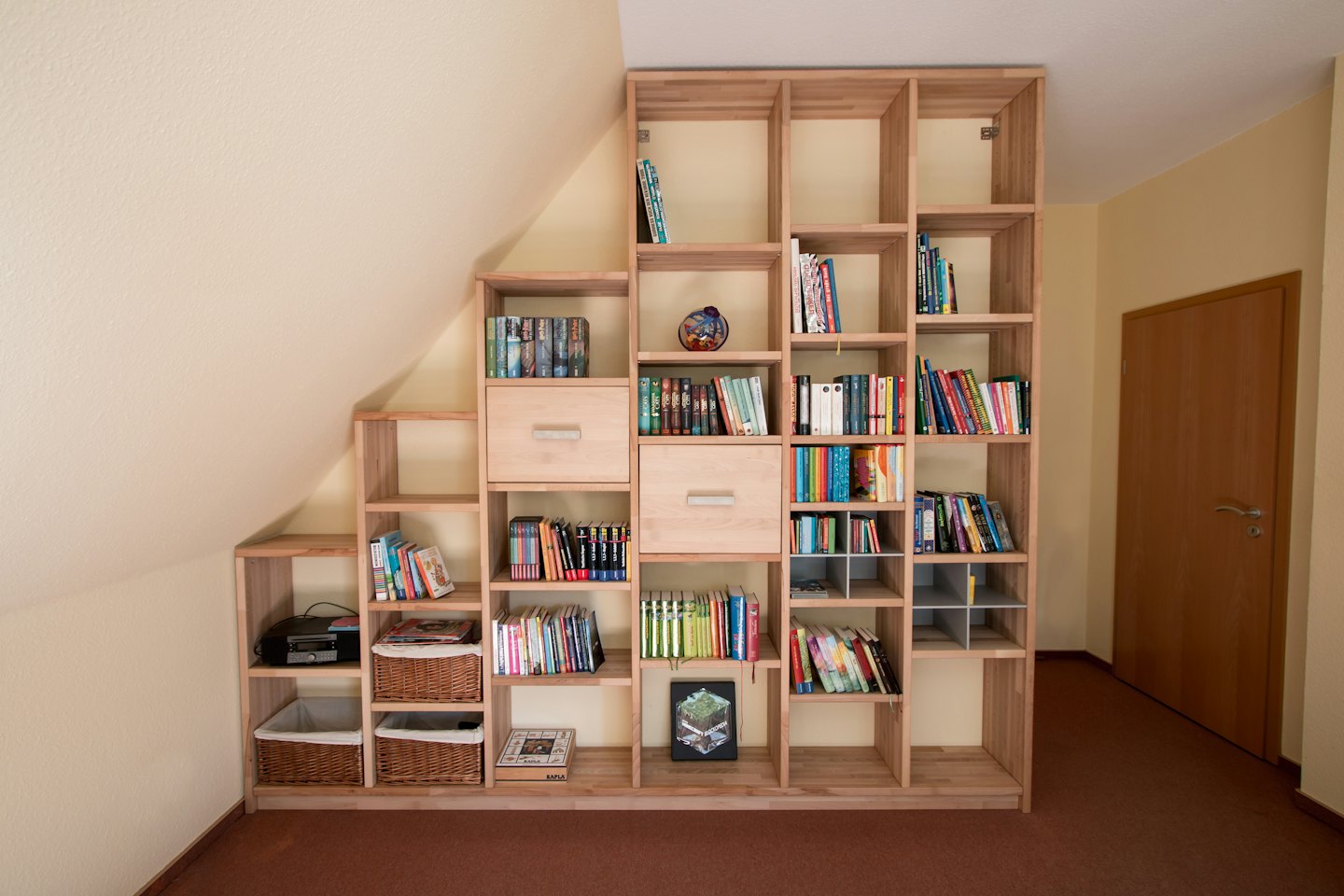 Libreria in legno su misura sotto un soffitto spiovente piena di libri.